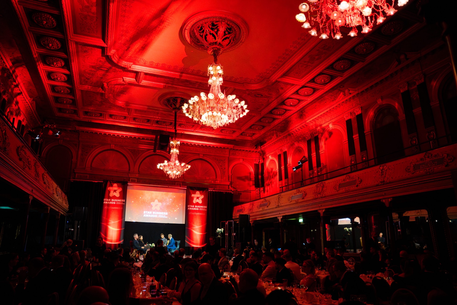 Star Business Awards-gala i en stor sal med kristallkronor och röd belysning